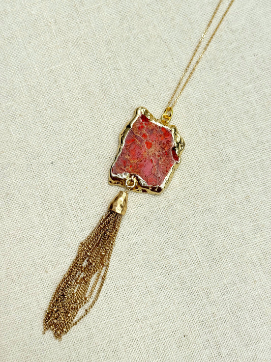 A gold-colored chain necklace with a red jasper pendant and a tassel pendant with a lobster clasp closure.