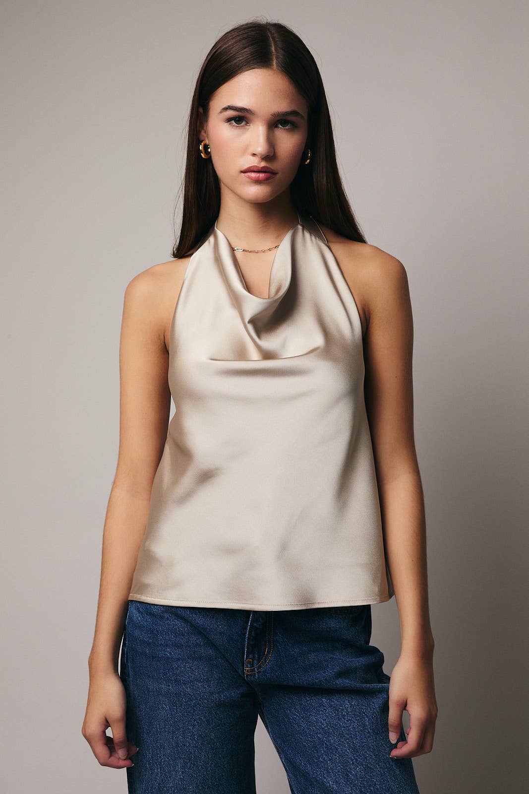 Woman wearing a beige halter top and blue jeans against a plain background