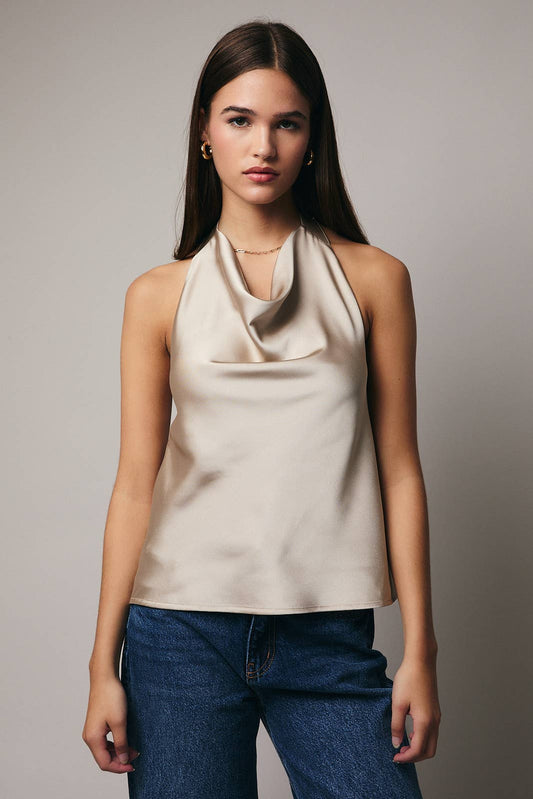 Woman wearing a beige halter top and blue jeans against a plain background